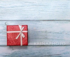 Christmas concept. Christmas greeting card with a red package on a teal table. Copy space on the right for your greeting message.