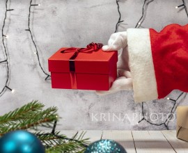 Santa Claus brings Christmas presents. Hand with white glove holding a gift box with paper and red ribbon.Christmas decorations all around.