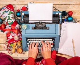 Christmas atmosphere with a vintage typewriter, stockings full of sweets, a red blanket and a pile of blank sheets.
