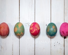 A homemade natural way to decorate Easter eggs. Five boiled eggs painted with colours, leaves and flowers on a shabby chic wooden table.
