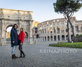 Young couple traveling to Rome. The young couple poses in front of the Arch of Titus. The blonde woman in her red jacket puts her hand on her boyfriend.