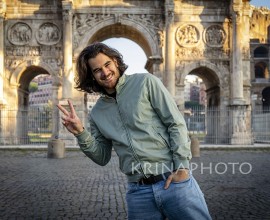 Happy moment in Rome. Young smiling man posing for a picture doing the V sign in front of the Titus arch.