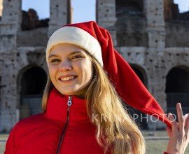 Roman holidays at Christmas. Beautiful blonde woman posing in front of the Colosseum with Santa Claus hat. The young woman looks into the camera and smiles.