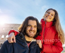 Young couple traveling to Rome. The couple smiles and takes a selfie in front of the Colosseum.