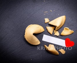 Fortune cookies on a black stone background with a little red heart. A broken cookie reveals a lovely message. Are you longing to read yours?