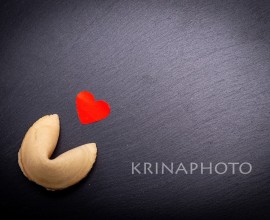 A fortune cookie with a little red heart on a black stone background. Are you ready to break the cookie and discover your love destiny?