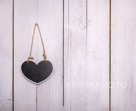 A small heart-shaped chalkboard hanging on a white wooden background. Write a sweet memo for your love.chalkboard hanging on a white wooden background. Write a sweet memo for your love.